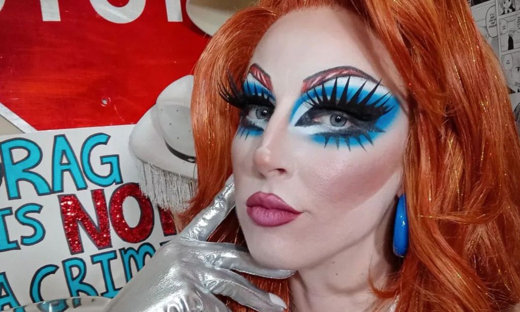 Tennessee drag queen Adhara Bull wears poses with one hand resting on their face with a sign in the background reading 'drag is not a crime' after the state banned drag in public places