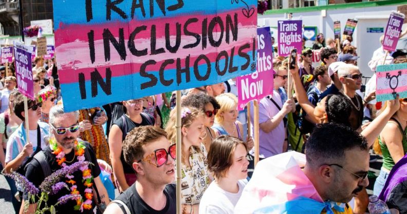 A crowd of people marching with a large trans flag with the words trans inclusion in schools