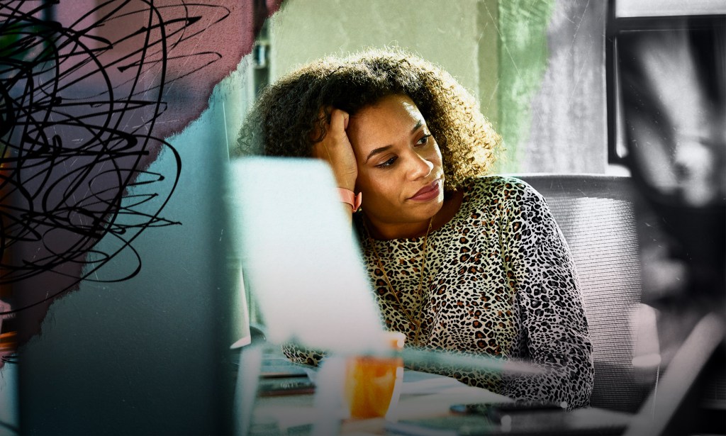 A Black woman is working from home. She is resting her head onto her right hand. She appears burnt out. 