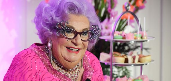 The late Barry Humphries dressed as his drag alter-ego Dame Edna Everage, with purple hair, horn-rimmed glasses and a pink dress