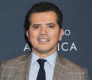 John Leguizamo posing in a plaid suit for a red carpet event.