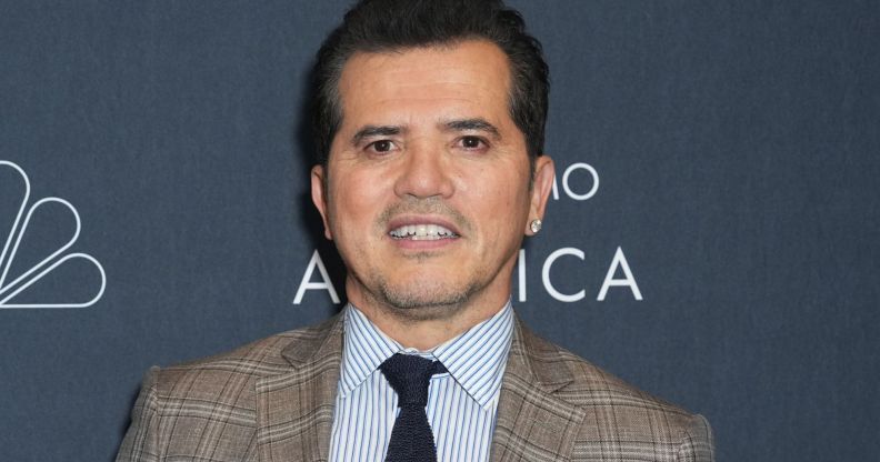 John Leguizamo posing in a plaid suit for a red carpet event.