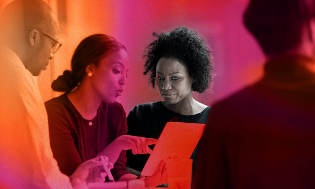 This is an image of two Black women having a conversation at work. They are both looking down at a tablet. There is a red and orange stylised background.