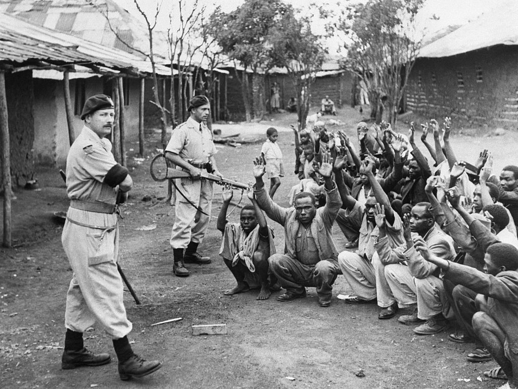 British policemen hold men from the village of Kariobangi at gunpoint while their huts are searched for evidence that they participated in the Mau Mau Rebellion of 1952. 