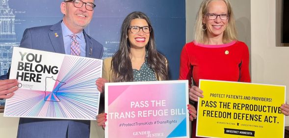 Minnesota lawmakers hold up signs of trans positivity.