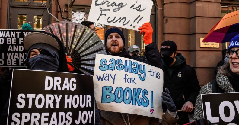 A person in a pro-drag rally holding signs reading 'drag story hour spreads joy'