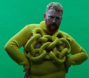 Non-binary, trans singer Tom Rasmussen wears a yellow sweater while standing in front of a green background