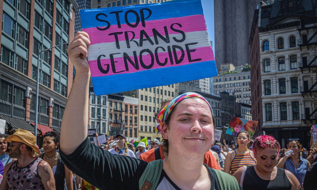 Trans protestor holding up a sign that reads "stop trans genocide"