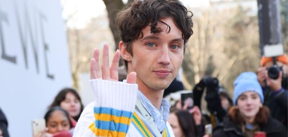 Singer Troye Sivan waves to the camera at 2023 Paris Fashion Week.