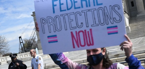 Protester holds up sign reading "federal protections now" with the trans flag