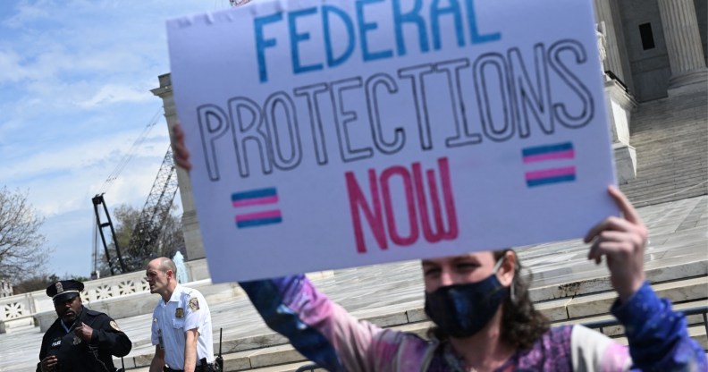 Protester holds up sign reading "federal protections now" with the trans flag
