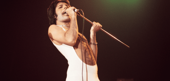Freddie Mercury wears a white outfit as he sings on stage during a performance with the band Queen
