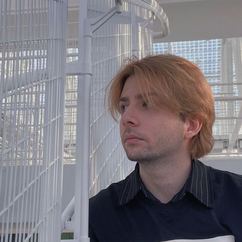 Gela Gogishvili, a LGBQ+ man living in Russia, sits on a stairway and stares somewhere off camera