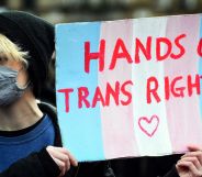 A person holds up a sign in the colours of the trans pride flag (blue, pink and white) reading 'hands off trans rights' amid a protest