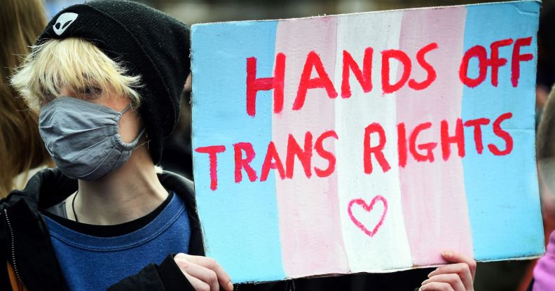 A person holds up a sign in the colours of the trans pride flag (blue, pink and white) reading 'hands off trans rights' amid a protest