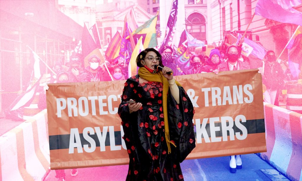 Trans activist Iman Le Caire speaks passionately into a microphone as she stands in front of a banner depicting its support for asylum seekers amid a march with a pink and blue wash over parts of the image