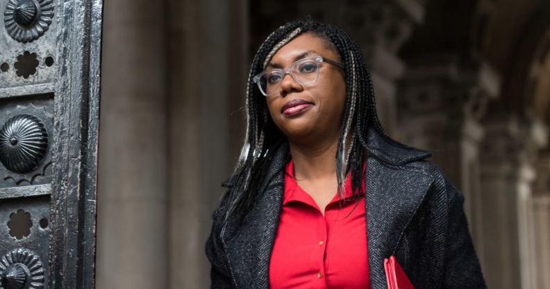 Kemi Badenoch wearing a black blazer and red blouse walking outdoors.