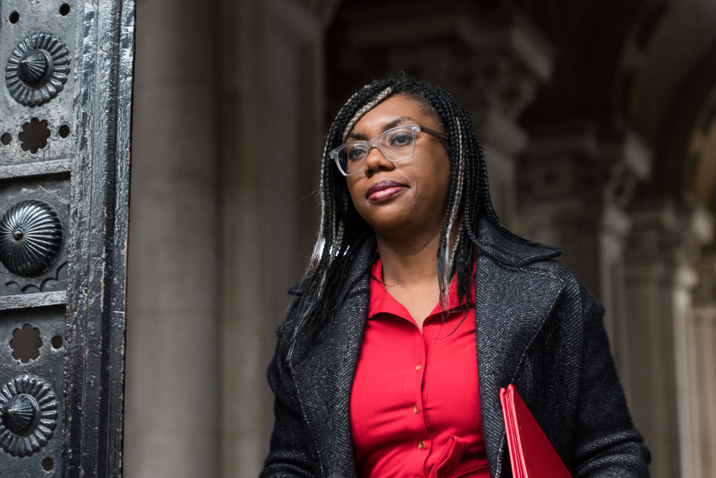 Kemi Badenoch wearing a black blazer and red blouse walking outdoors.