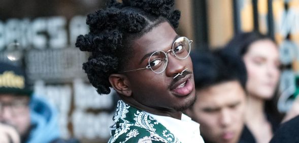 Rapper Lil Nas X wears a green and silver patterned jacket, round silver glasses and a nose piercing