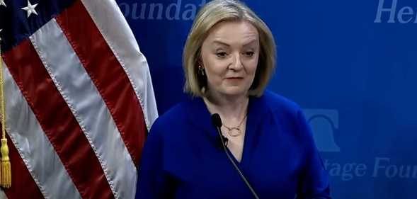 Liz Truss speaking in front of a US flag