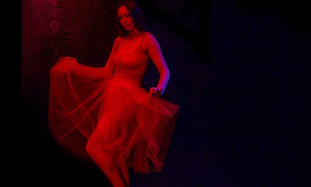 Maggie, cast in red light, dancing in a sheer skirt
