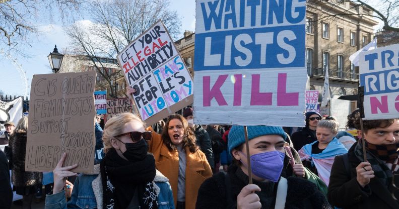 A person holds up a sign in the colours of the trans Pride flag (blue, pink and white) reading 'Waiting lists kill' referring to the huge wait times trans people face accessing gender-affirming healthcare on the NHS