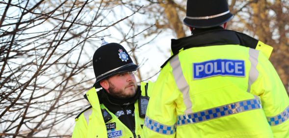 Two police officers wear the yellow, blue and black uniforms associated with law enforcement in England and Wales as they stand at the scene of a crime