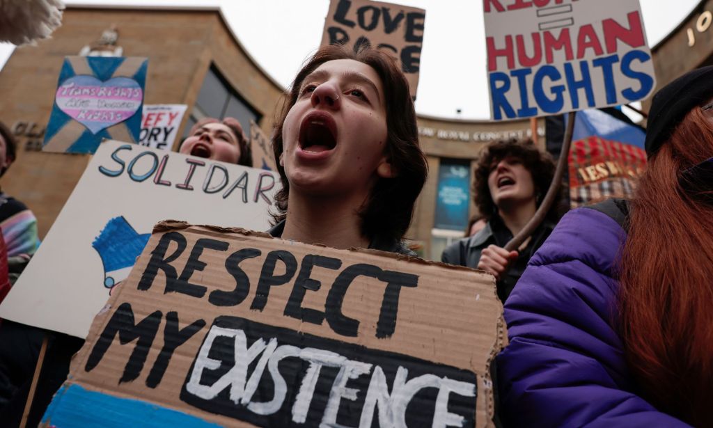 A person holds up a sign reading 'respect my existence' during a protest in favour of trans rights and against the Tory government