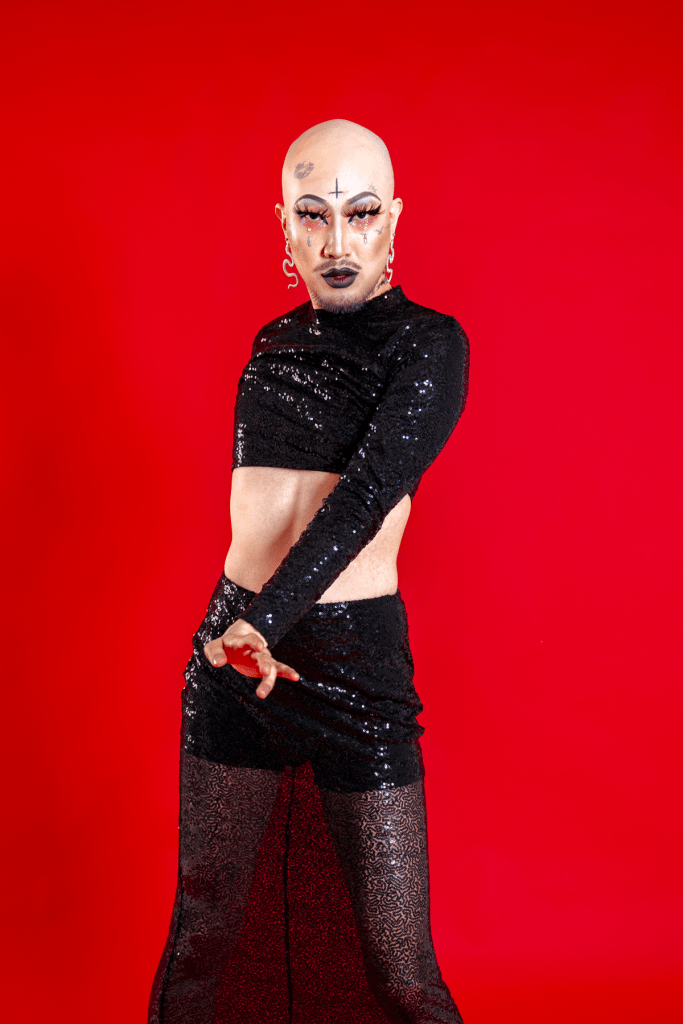 South Korean LGBTQ+ activist Heezy Yang is dressed, as his drag persona Hurricane Kimchi, in a black outfit with a red background