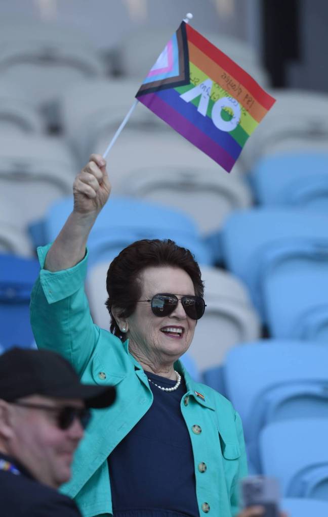 Tennis legend Billie Jean King waves a progressive Pride LGBTQ+ flag while sitting in chairs during a match