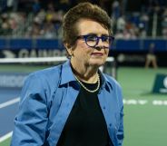 Tennis legend Billie Jean King wears a dark shirt and blue jacket as she stands on a tennis court