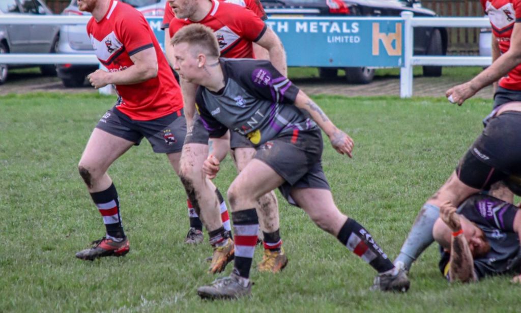 Trans man Jordan Blackwood wears a grey, black and purple rugby uniform as he runs on the pitch during a game with the Newcastle Ravens