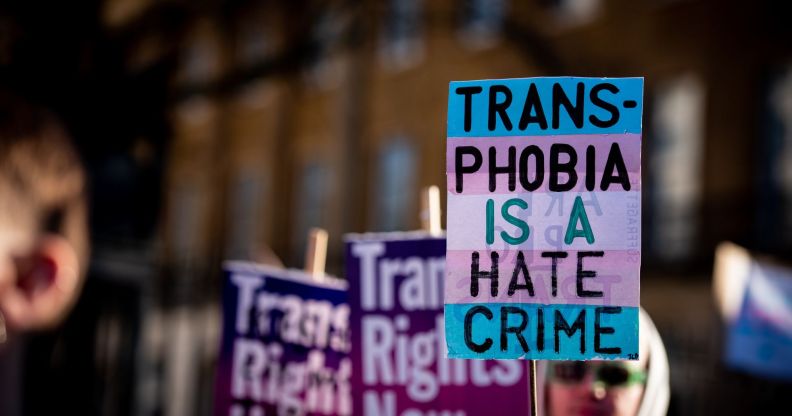 A person holds up a sign in the colours of the trans pride flag (blue, pink and white) reading 'Transphobia is a hate crime' during a protest