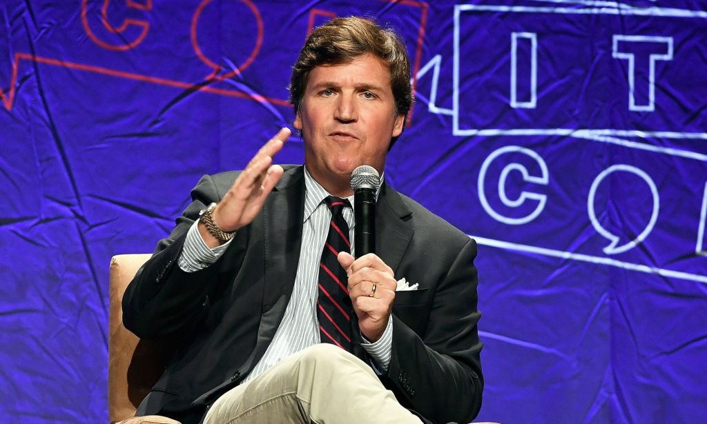 Tucker Carlson, who is infamous for making anti-trans, anti-LGBTQ+ statements on his Fox News show, wears a suit and tie as he speaks at Politicon 2018