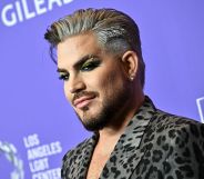 Singer Adam Lambert wears an animal-print shirt and stands against a purple background