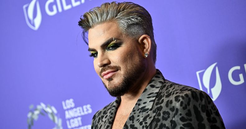 Singer Adam Lambert wears an animal-print shirt and stands against a purple background