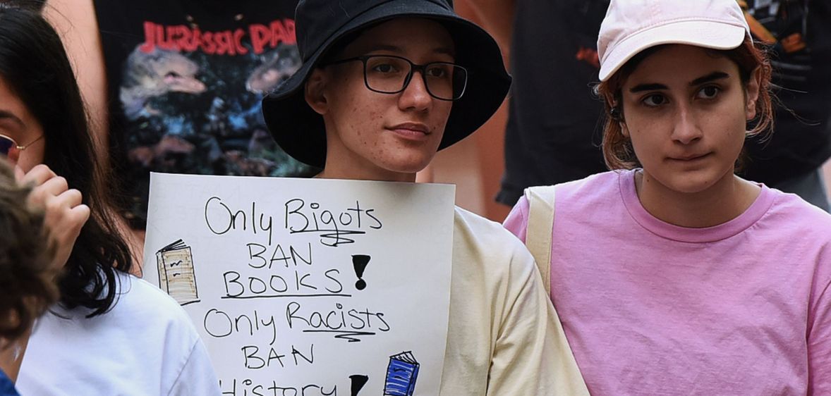 A person holds a sign reading "only bigots ban books, only racists ban history."