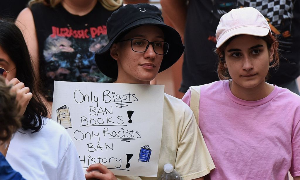 A person holds a sign reading "only bigots ban books, only racists ban history."