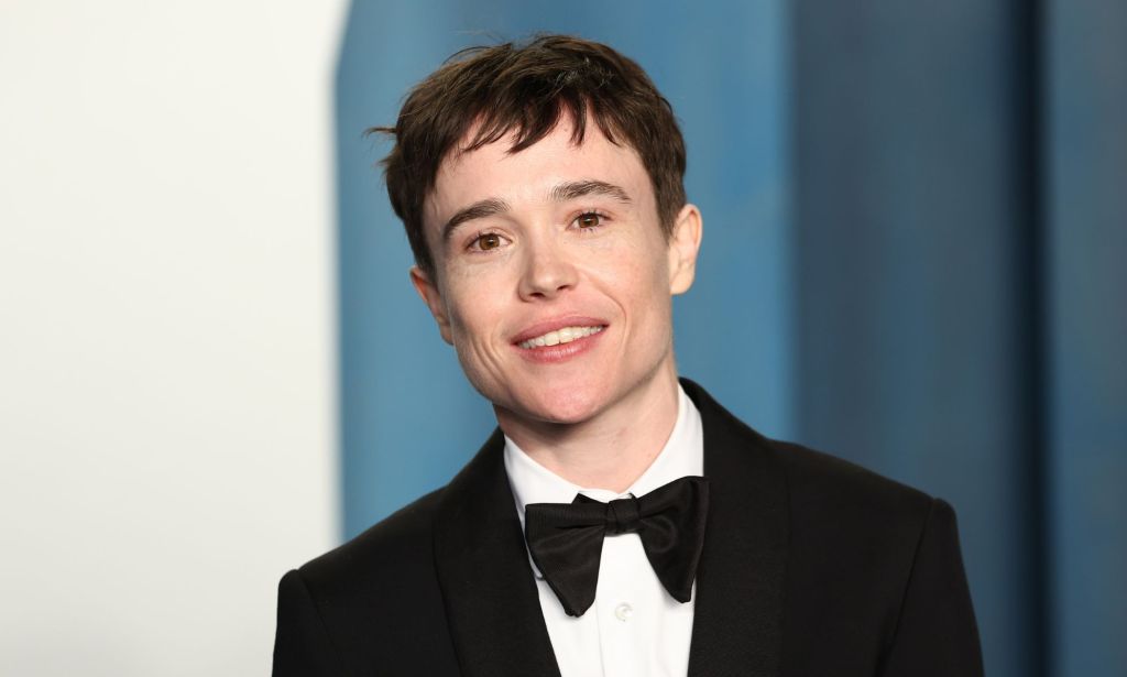 Elliot Page wears a black suit and bow tie while smiling at the camera.
