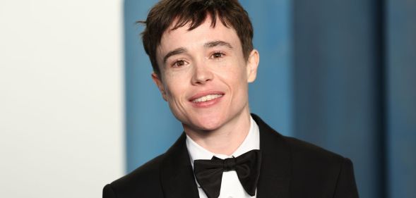 Elliot Page wears a black suit and bow tie while smiling at the camera.