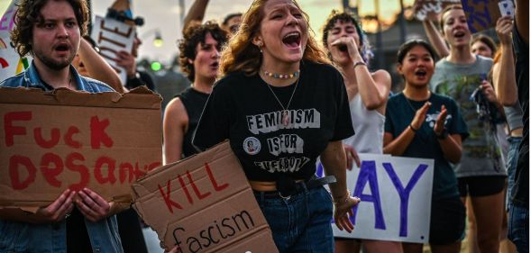 Protestors condemning Ron DeSantis' LGBTQ+ tirade in Florida, with signs reading "fuck DeSantis" and "kill fascism."