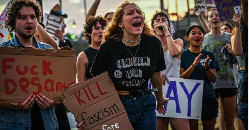 Protestors condemning Ron DeSantis' LGBTQ+ tirade in Florida, with signs reading "fuck DeSantis" and "kill fascism."