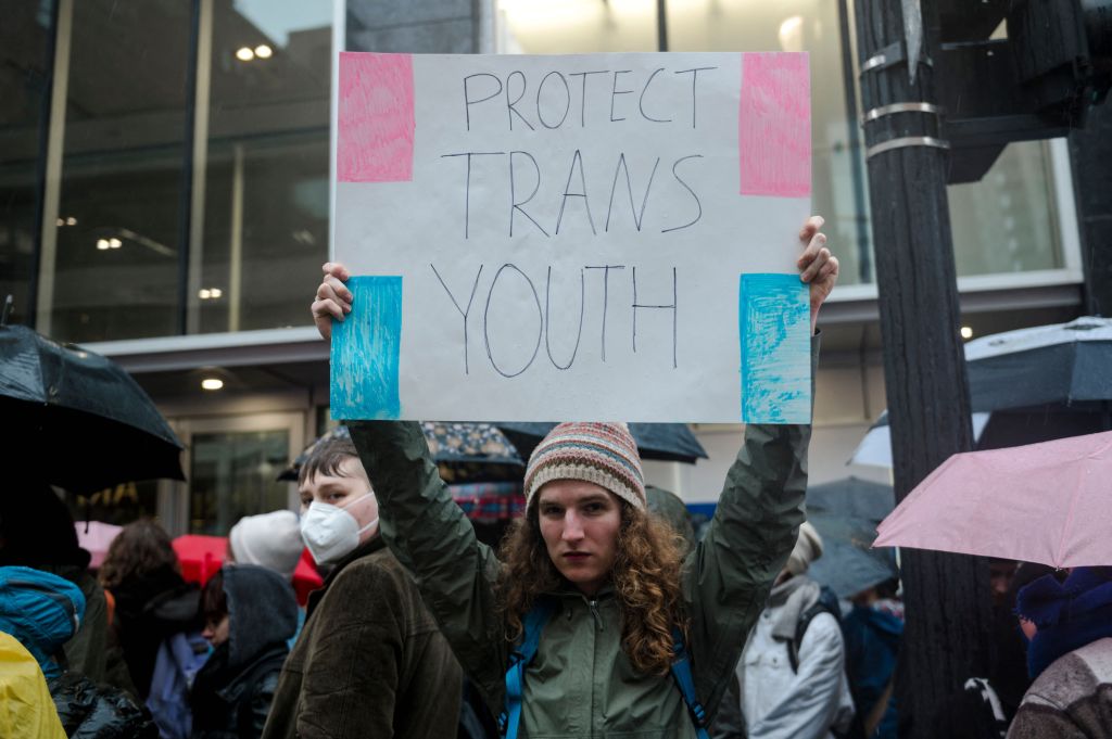 Man holds sign reading "protecting trans youth"