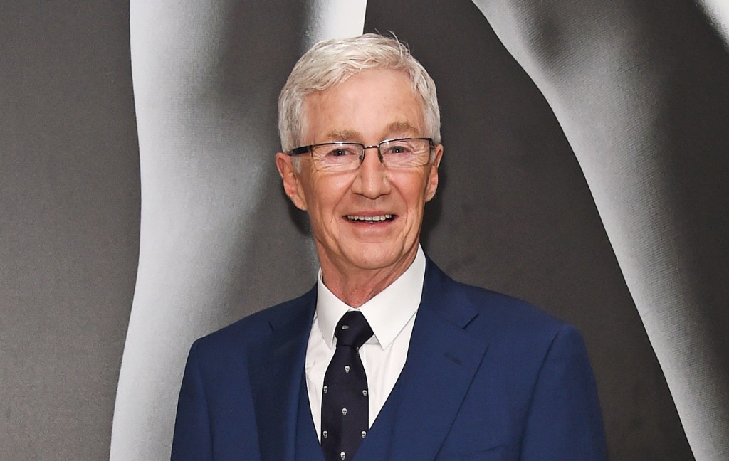 Paul O’Grady wearing a blue suit on a grey background