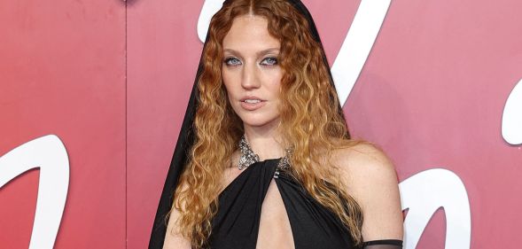 Jess Glynne wears a black dress with chest cutout and black hood.