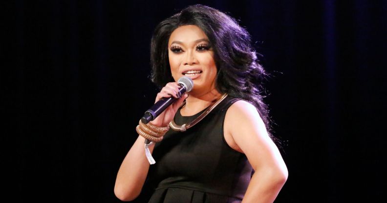 RuPaul's Drag Race queen Jujubee wears a dark wig and dress while smiling and speaking into a microphone.
