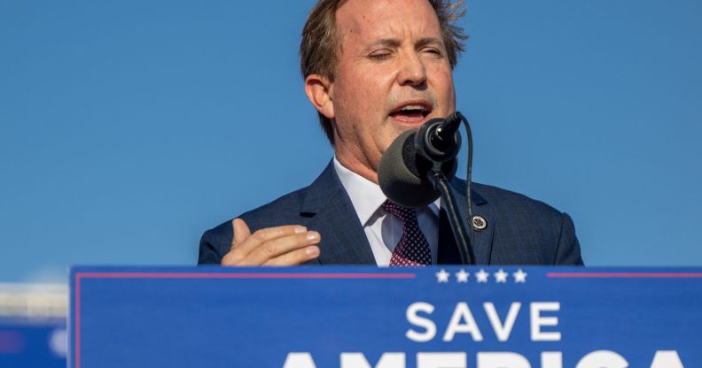 Ken Paxton speaking to a crowd, with a sign reading "save America" below him.