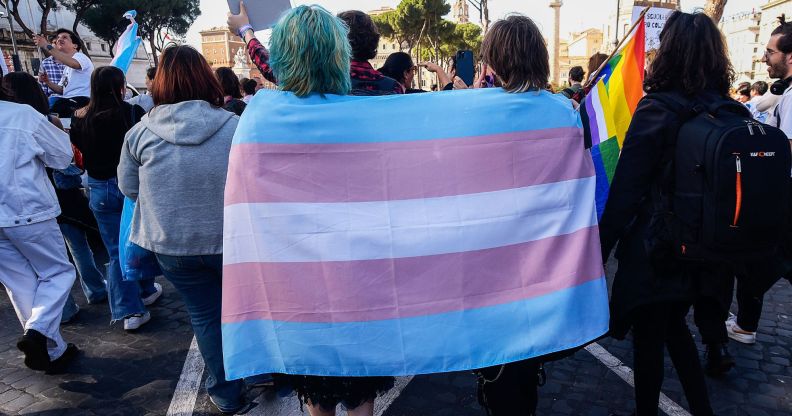 Two trans activists huddle together under a trans Pride flag.