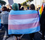 Two trans activists huddle together under a trans Pride flag.