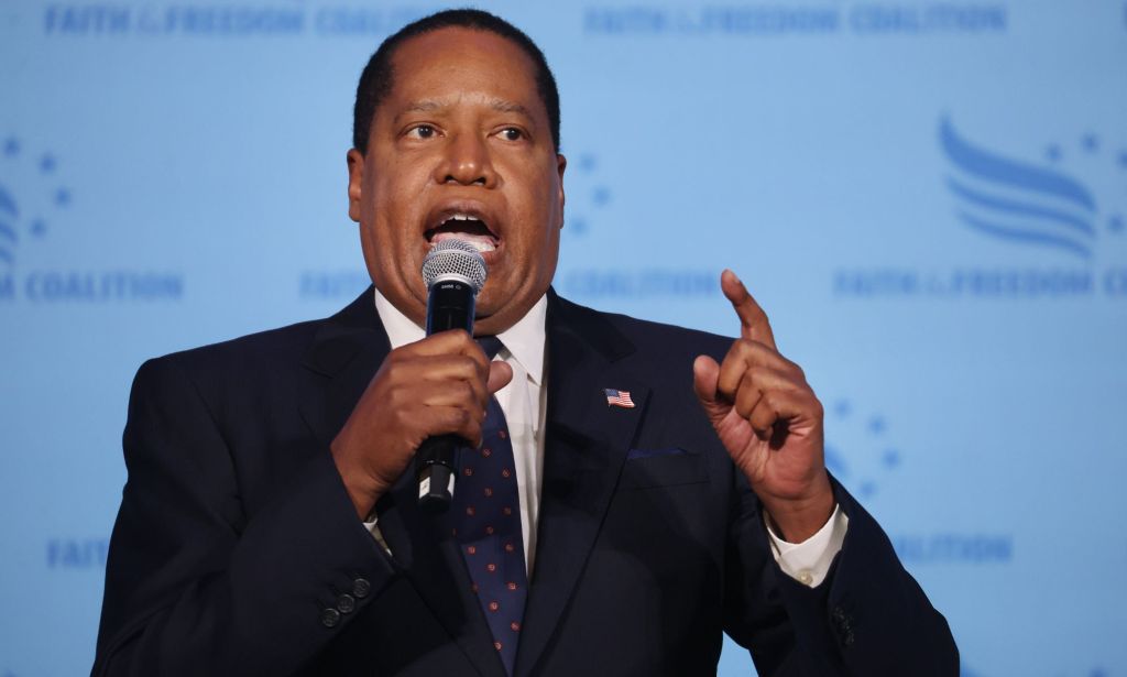 Larry Elder, who is a 2024 Republican presidential candidate, wears a white shirt and dark jacket as he speaks into a microphone and gestures with one had during a conservative, religious conference